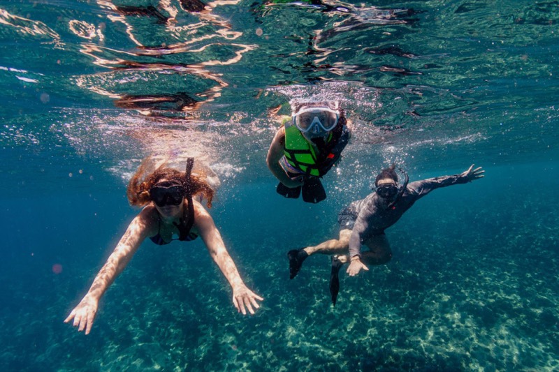 Three people snorkeling over the reef